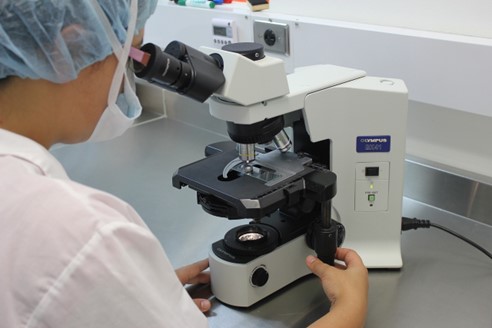 persona con camice in un laboratorio di scienze che osserva al microscopio